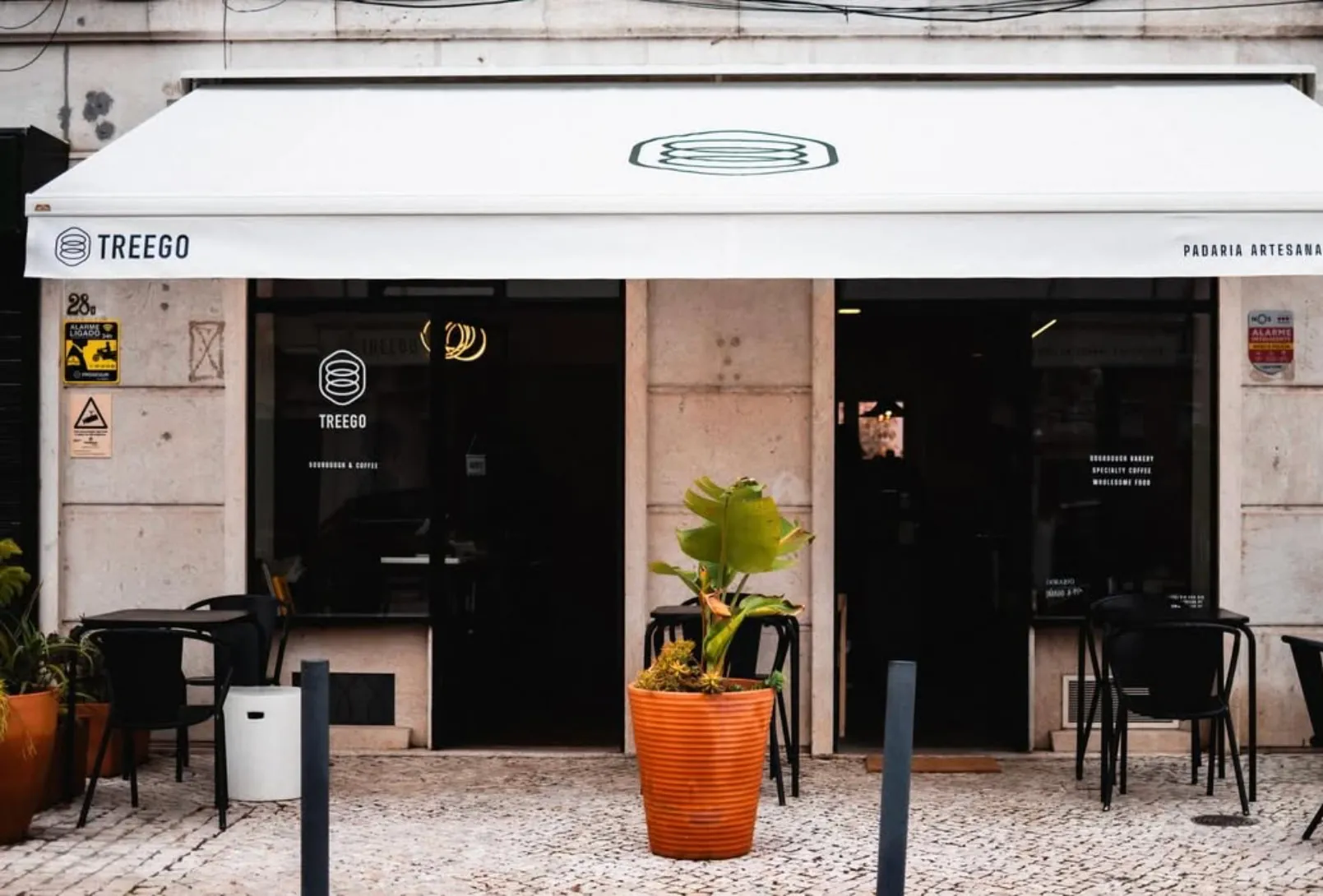 A montra da Treego na Avenida de Roma 28B, com o toldo branco, a esplanada e o vaso de terracota.